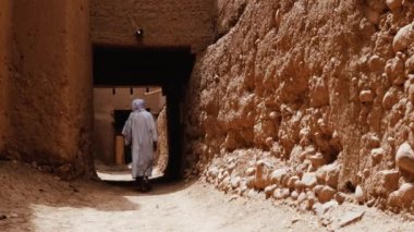 Beyaz gandoura giyen geleneksel giyimli Faslı bir Bedevi adam Tamnougalt, Fas 'ta bir Kasbah' ın içinde yürüyor. Güney Fas 'ın otantik kırsal manzarası. 4k. 