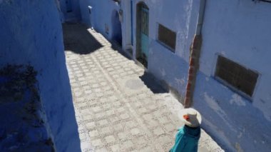Chefchaouen, Tetouan, Fas - 28 Temmuz 2022: Fas 'ın başkenti Chefchaouen' de geleneksel giyinmiş bir kadınla sokak sahnesi. Ünlü, popüler turist gezisi merkezi. 4k görüntü.