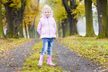 Kauçuk giymiş küçük kız sonbahar sokakta önyükleme yapar.