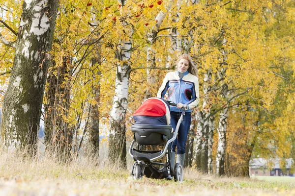 Kvinna med barnvagn på promenad i höstliga naturen — Stockfoto