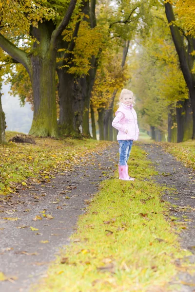 Liten flicka klädd i gummi stövlar i höstlig gränd — Stockfoto