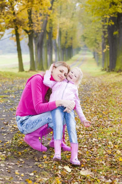 Mother and her daughter with umbrellas in autumnal alley — Stock Photo, Image