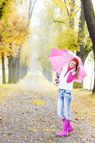Mujer con botas de goma y paraguas en callejón otoñal — Foto de Stock