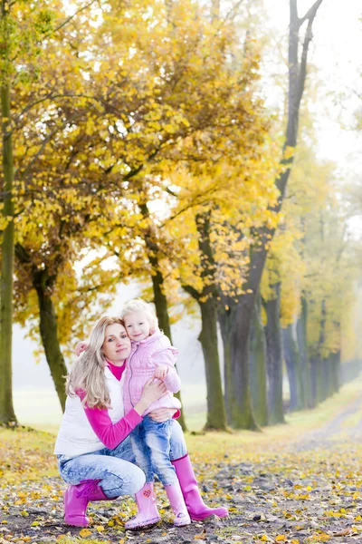 Mother and her daughter with umbrellas in autumnal alley — Stock Photo, Image