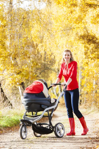 Mor och hennes dotter med barnvagn på promenad i höstlig gränd — Stockfoto