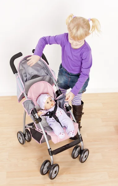 Kleines Mädchen spielt mit einer Puppe und einem Kinderwagen — Stockfoto