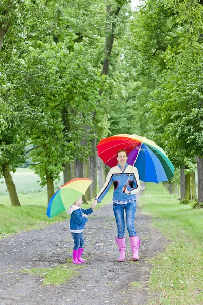 Mother and her daughter with umbrellas in spring alley — Stock Photo, Image
