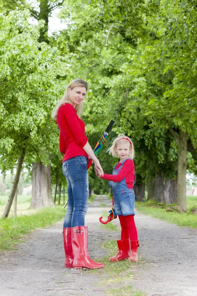 Mother and her daughter with umbrellas in spring alley — Stock Photo, Image