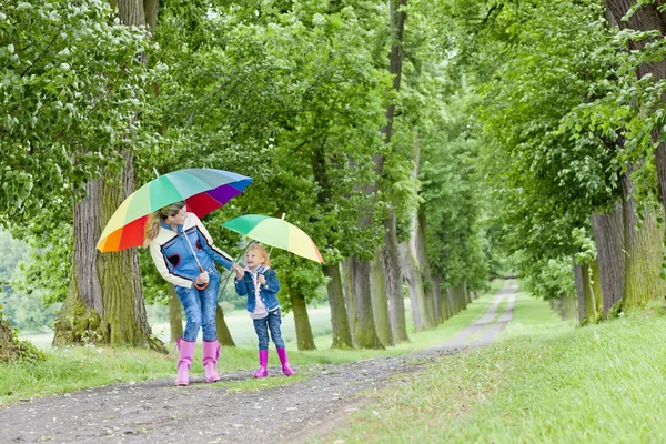 Mother and her daughter with umbrellas in spring alley — Stock Photo, Image