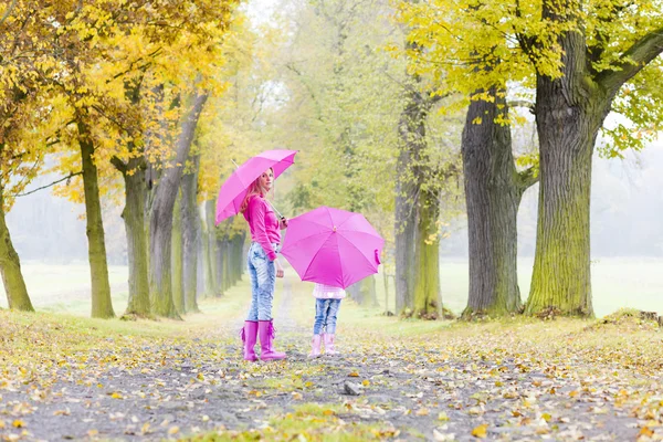 Moeder en haar dochter met paraplu's in herfst steegje — Stockfoto