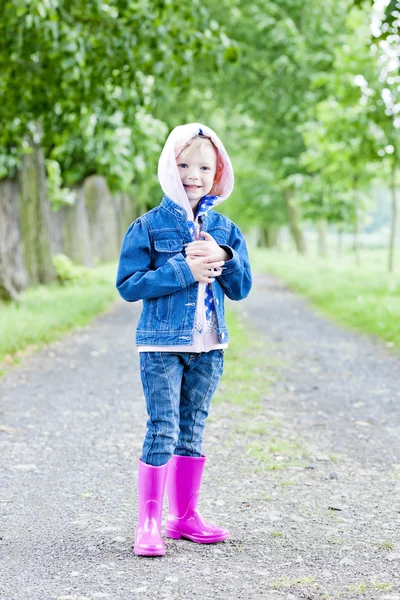 Liten flicka klädd i gummi stövlar i våren gränd — Stockfoto