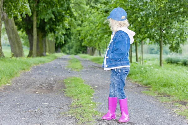 Liten flicka klädd i gummi stövlar i våren gränd — Stockfoto