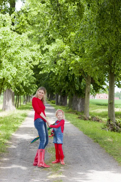 Moeder en haar dochter met parasols in voorjaarssteegje — Stockfoto