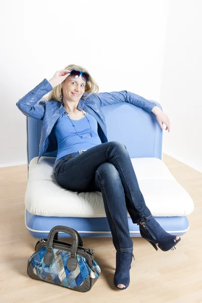 Kobieta nosi niebieskie stroje z torebki, siedząc na kanapie — Zdjęcie stockowe