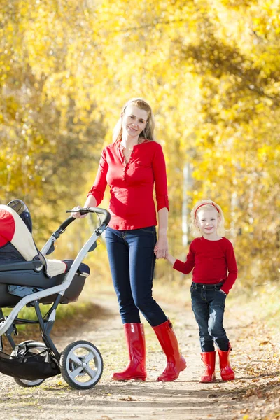 Mor och hennes dotter med barnvagn på promenad i höstlig gränd — Stockfoto