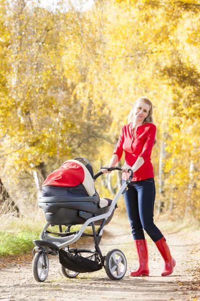 Kvinna med barnvagn på promenad i höstlig gränd — Stockfoto