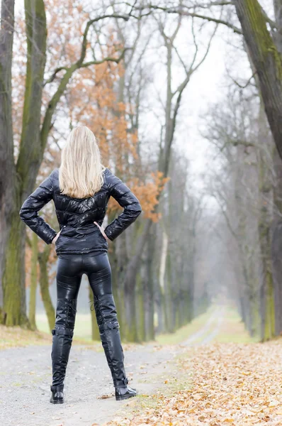 Γυναίκα, φορώντας μαύρα ρούχα και μπότες σε φθινοπωρινό δρομάκι — Φωτογραφία Αρχείου