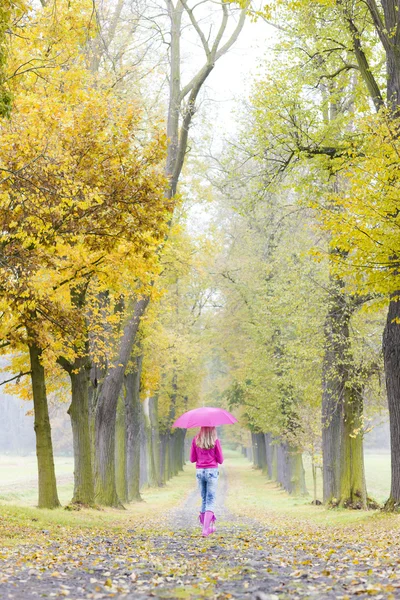 Frau trägt Gummistiefel mit Regenschirm in herbstlicher Gasse — Stockfoto