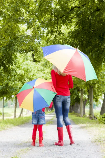 Mother and her daughter with umbrellas in spring alley Stock Picture