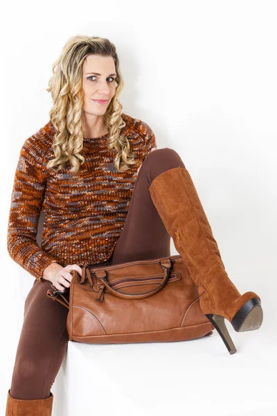 Sitting woman wearing brown clothes and boots with a handbag — Stock Photo, Image