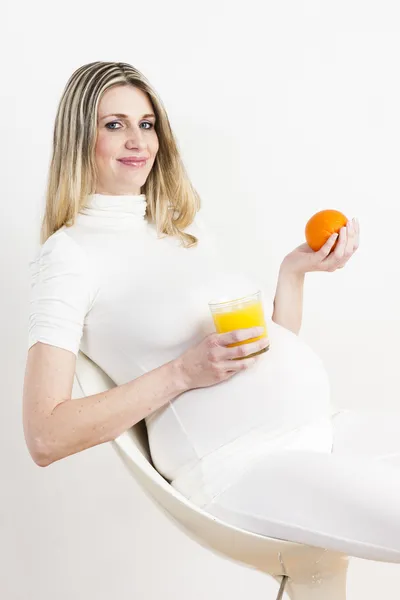 Gravid kvinna med ett glas apelsinjuice och en orange — Stockfoto