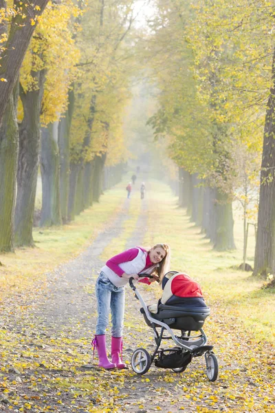 紅葉の路地で散歩に pram を持つ女性 — ストック写真