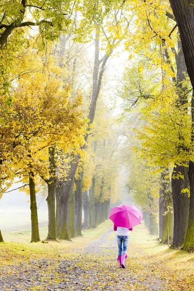 Žena nosí gumové boty s deštníkem v podzimních uličce — Stock fotografie