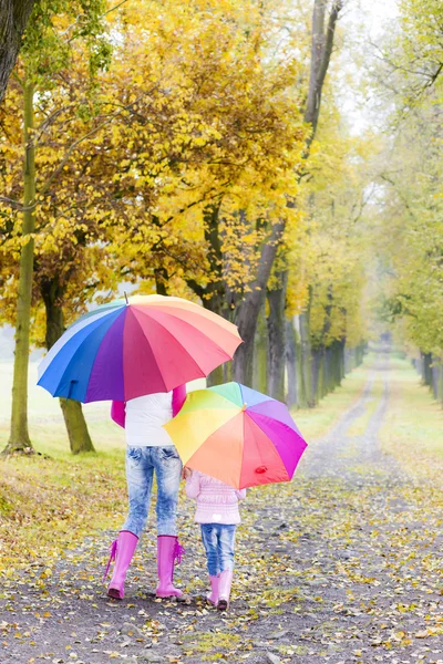 Mother and her daughter with umbrellas in autumnal alley Stock Image