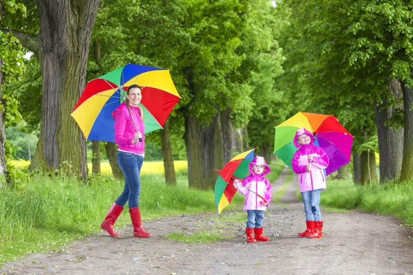 Moeder en haar dochters met paraplu's in voorjaar steegje — Stockfoto