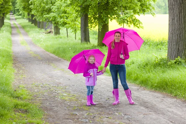 Mother and her daughter with umbrellas in spring alley — Stock Photo, Image