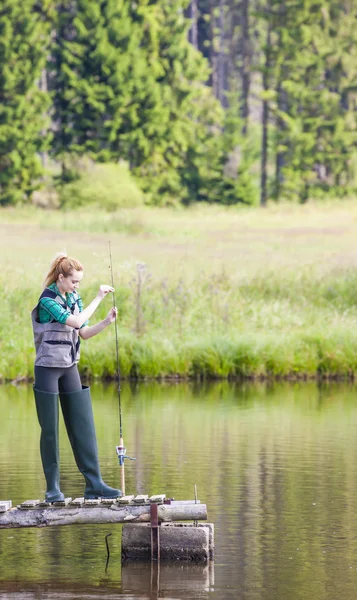 Young woman fishing on pier at pond — Stock Photo, Image