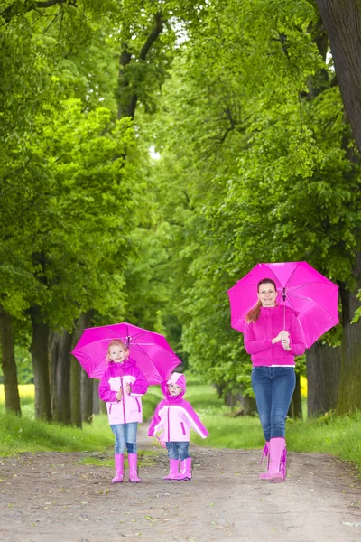 Mother and her daughters with umbrellas in spring alley — Stock Photo, Image