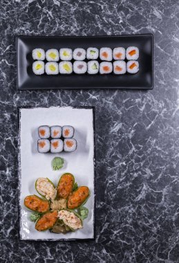 Siyah taşlı arka planda deniz mahsullü suşi ruloları.