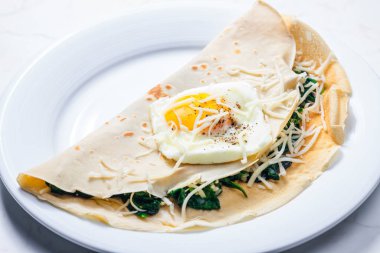 Kızarmış yumurta ve rendelenmiş peynirle servis edilen ıspanak yapraklarıyla doldurulmuş krep.