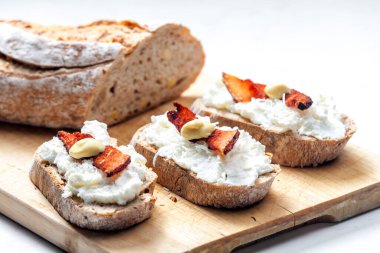 Domuz pastırması, rendelenmiş peynir ve hardalla servis edilen bir dilim ekmeğe sarımsak sürülmüş.