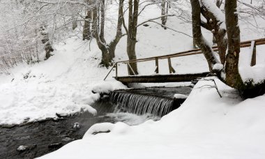 Kar yağışı sırasında nehirdeki ahşap köprü. Karpatlar, Ukrayna