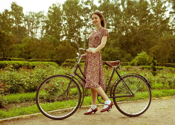 Giovane donna in abito in posa con bicicletta retrò nel parco . — Foto Stock