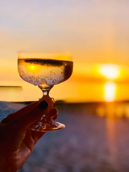 Mulher de colheita segurando copo de champanhe na praia ao pôr-do-sol — Fotografia de Stock