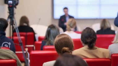 Konuşma sırasında kameranın yanında oturan iş semineri katılımcıları