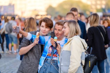 Kalabalık meydanda dondurmayla selfie çeken kadınlar.