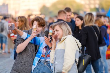 Kalabalık meydanda dondurmayla selfie çeken kadınlar.
