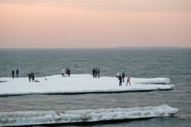 People admiring sea from snowy shore