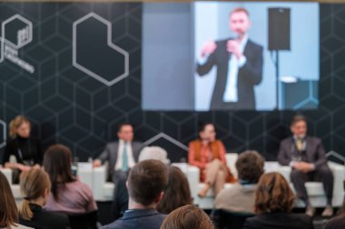 Kalabalık salonda oturan ve konferans sırasında çevrimiçi uzaktan konuşmacının sunumunu dinleyen bir grup iş adamının arka planı