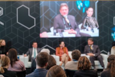 Kalabalık salonda oturan ve konferans sırasında çevrimiçi uzaktan konuşanların sunumunu dinleyen bir grup iş adamının arka planı