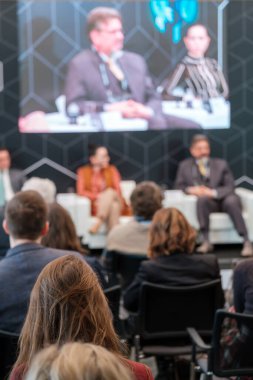 Kalabalık salonda oturan ve konferans sırasında çevrimiçi uzaktan konuşanların sunumunu dinleyen bir grup iş adamının arka planı