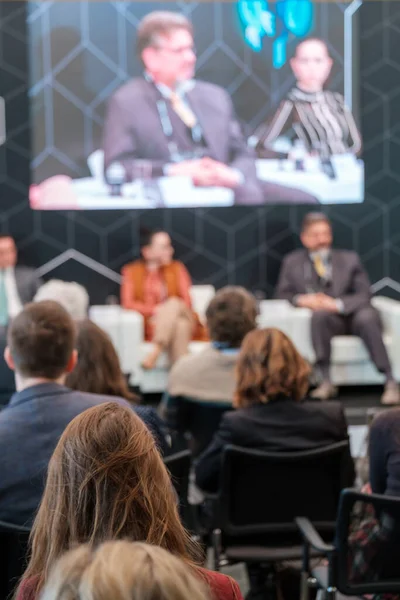 Kalabalık salonda oturan ve konferans sırasında çevrimiçi uzaktan konuşanların sunumunu dinleyen bir grup iş adamının arka planı