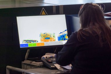 Havaalanında çalışırken bilgisayar ekranındaki çantaları kontrol eden uzun siyah saçlı, isimsiz bir kadın çalışan.