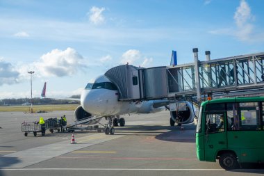 Moskova - 12 Mayıs 2022: Çalışanlar havaalanındaki bulutlu mavi gökyüzüne kargo yüklerken jet köprüsü ve otobüsün yanına park edilmiş modern uçak