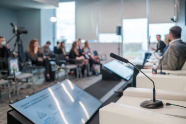 Tanımlanamayan erkek ve kadın hoparlörlerin resmi kıyafetleriyle mikrofon ve monitörlerin yanındaki koltuklarda otururken konferans salonundaki iş konferansında konuşurken yan görünümü