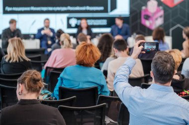 Modern salondaki iş semineri sırasında sandalyelerde oturan ve hoparlörleri dinleyen isimsiz insanların arka plan görüntüsü.